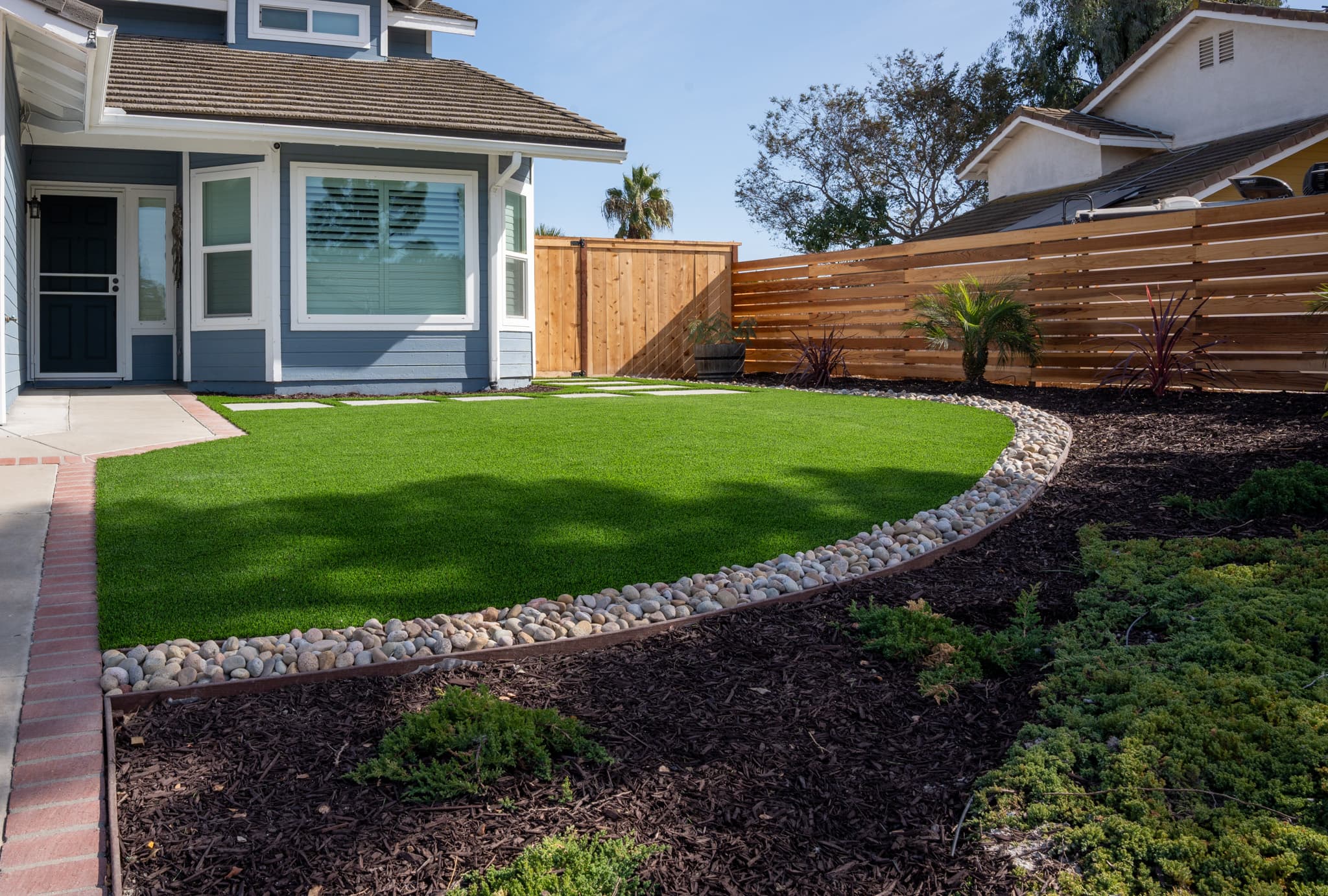 Contemporary landscaping featuring river rocks, palm trees, and mulch beds.