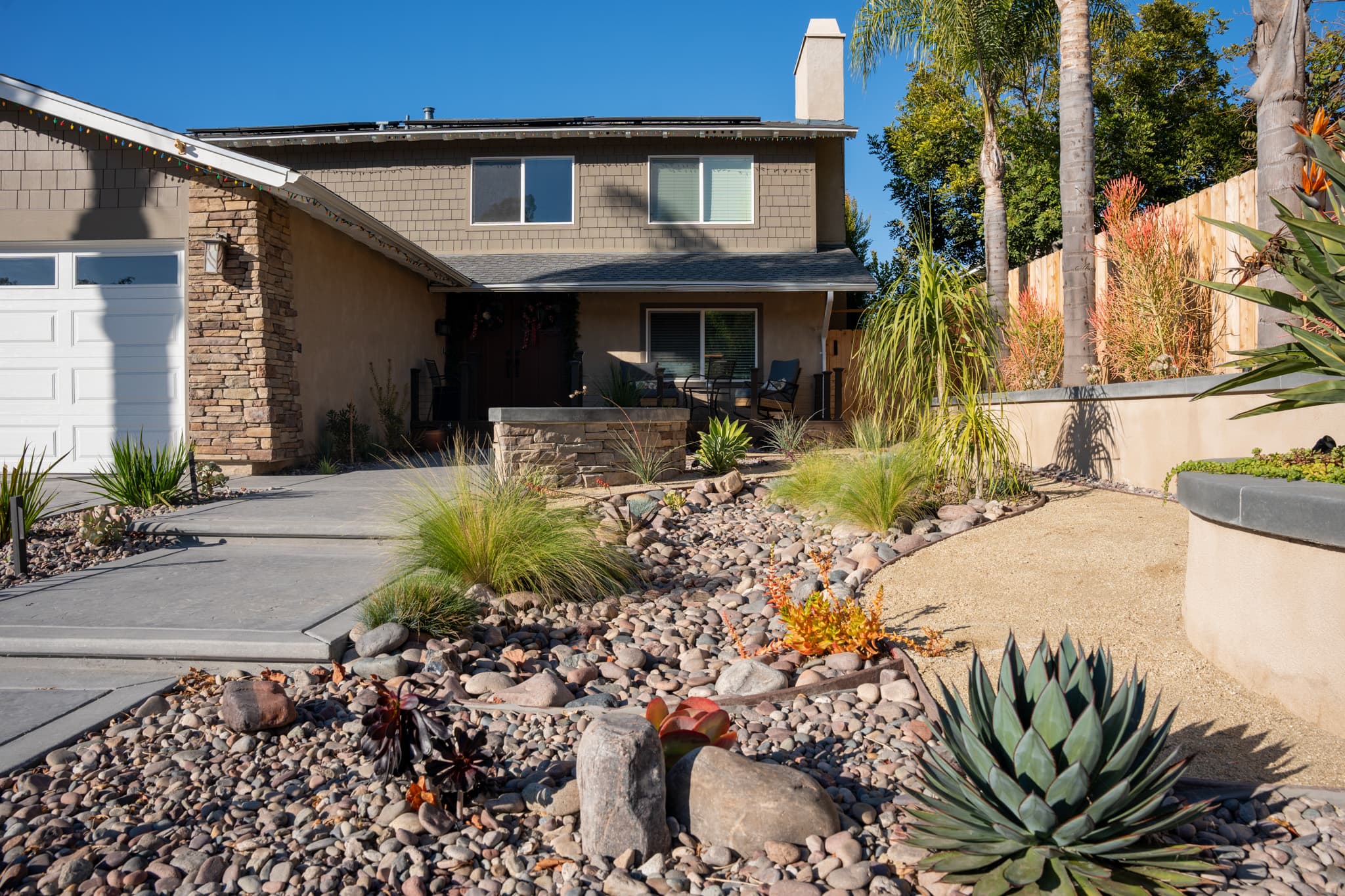 Front yard with xeriscape design featuring agave, palms, and river rocks
